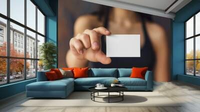 a hand and arm holding out an empty white business card with no text or design. The woman wears a black tank top with a blurred background Wall mural