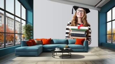 Young graduated student looking away and carrying books on gray background Wall mural