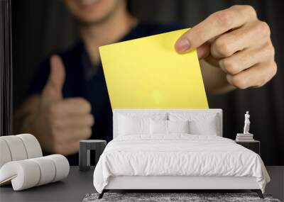 Man holds blank yellow sticker. Thumb up, blue T-shirt. close-up, selective focus Wall mural