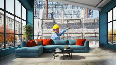 asian male engineer or foreman wearing safety helmet working at construction site or building site of highrise building. Wall mural