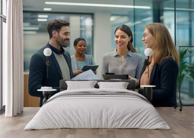 A group of four diverse business professionals stand in an office hallway, smiling and engaging in conversation.  They hold files and tablets.  They are all dressed in business casual attire. Wall mural