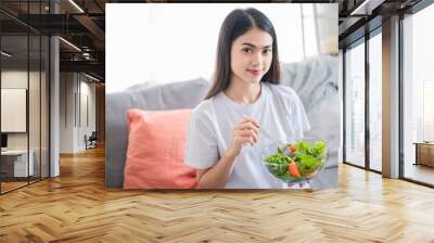 Beautiful Asian woman are eating fresh salad she look fresh and healthy. She sit in her clear living room. New normal self care, good food for life, beauty, diet food concept. Wall mural