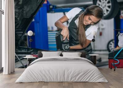 Beautiful Mechanic  girl in a black jumpsuit and a white T-shirt changes the oil in a black car. car repair concept Wall mural