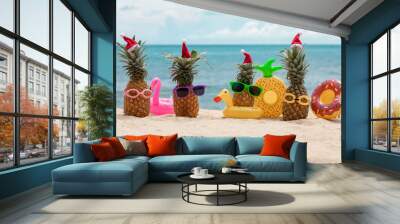 Family of funny attractive pineapples in stylish sunglasses on the sand against turquoise sea. Wearing christmas hats. Christmas and new year vacation concept on tropical beach. Family holiday. Bright Wall mural