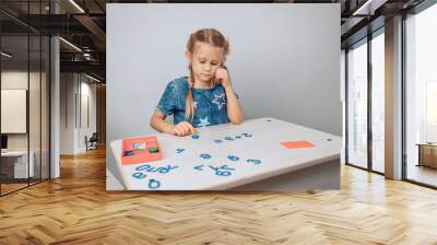 Portrait of a smart pretty girl sitting at a white table drawing and raising her finger up. New idea. Child development. Childhood concept. photo with noise Wall mural