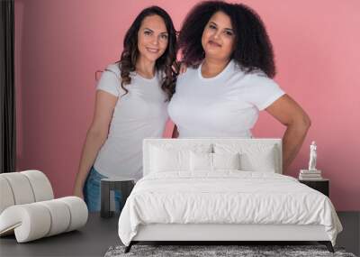 Two cute girls an African American and a Caucasian girl smile directly at the camera in white t shirts on a pink background Wall mural