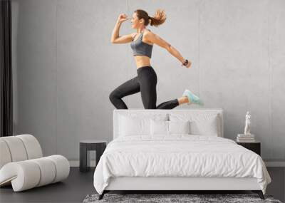 Beautiful sportwoman with pony tail, healthy skin, jumps in air, dressed in casual top and leggings, poses over grey background, wears smartwatch. Slim athleteic girl has gymnastics. Healthy lifestyle Wall mural