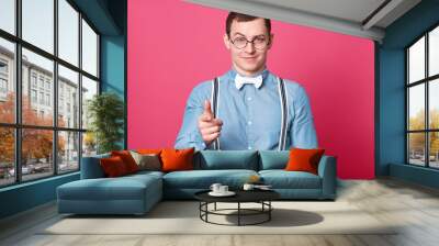 Charismatic confident handsome young man looks directly at camera, raise one eyebrows, shows direction with his forefinger, looks animated. Smiling magnetic guy poses isolated over pink background. Wall mural