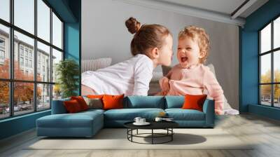 Charming siblings having fun at home, happy little girls playing in bedroom, cute positive children rejoicing enjoying lazy morning having fun together. Wall mural