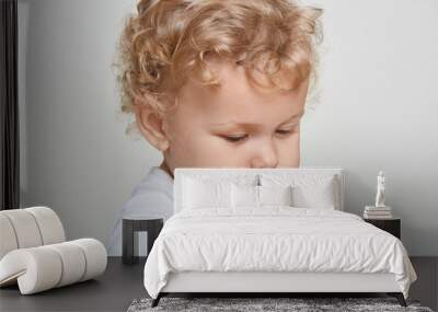 Close up portrait of baby boy looking away, infant has blond curly hair, wearing casual shirt, posing isolated over white background, charming toddler with bunting cheeks and lips. Wall mural