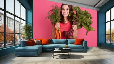 Closeup portrait of smiling female after harvestng, young gardener with carrot and beetroots in hands looking smiling at camera, woman vegetarian wearing casual red t shirt, girl with dark hair. Wall mural