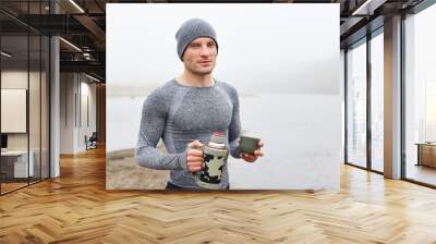 Handsome attractive man at lake bank with foggy river on background, young guy wearing gray closing posing with foggy river on background, looks at camera with calm expression. Wall mural