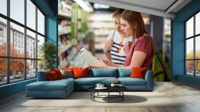 indoor shot of two young female companions come in store for buying necessary products, hold milk, c Wall mural