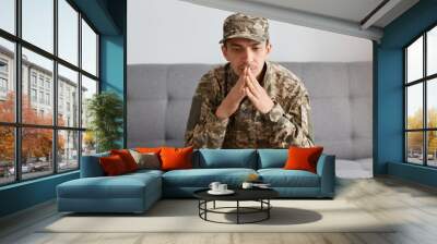 indoor shot of unhappy soldier man in camouflage uniform and cap keeping hand near face while sittin Wall mural