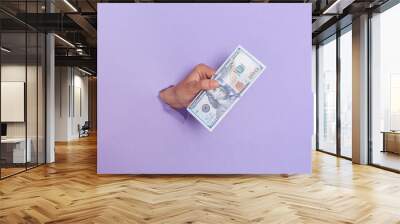 One hundred dollar banknotes in human's hand breaking through purple paer wall, unknown hand, reaching out with money, proposing money, paying, and offering us banknotes. Wall mural