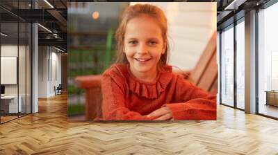 outdoor portrait of smiling little girl sitting near her house looking at camera with cheerful smile Wall mural