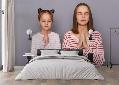 Portrait of calm relaxed mother and daughter wearing casual clothes standing isolated over gray background, keep palms together, praying or practicing yoga. Wall mural