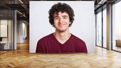 Positive pleased male with curly hair, looks happy at camera, has satisfaid facial expression, dresses in casual outfit. Model poses isolated over white background. Free spase for your logo. Wall mural