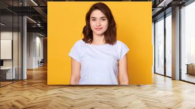 Studio portrait of beautiful young woman with dark hair. Pretty model girl with perfect fresh clean skin looking directly at camera with charming smile, slim female having happy facial expression. Wall mural