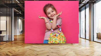 Studio shot of cute charming little lady wearing casual outfit and different multicolored jewelry, keeping hands near face, looking smiling directly at camera, having funny facial expression. Wall mural