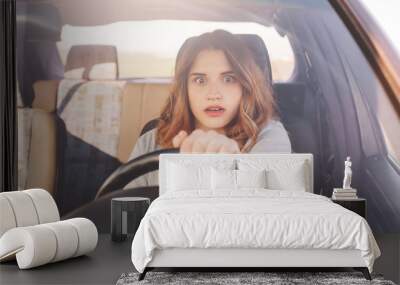 Terrified young cute female looks with depressed scared expression in front as drives car, has collision with other transport or accident on road, being inexperienced driver. Problems on road Wall mural