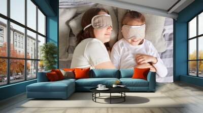 Top view of mother lying on pillow with daughter, wearing blindfolds, resting in morning in bedroom, sleeping hugging in bed, lazy weekend. Wall mural