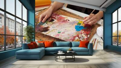 Unrecognizable woman painter wearing brown apron in art studio drawing picture using colorful paints drawing abstract work of art closeup hands with paintbrush Wall mural