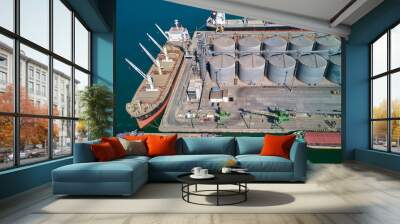 Loading grain into holds of sea cargo vessel in seaport from silos of grain storage. Bunkering of dry cargo ship with grain. Aerial top view Wall mural