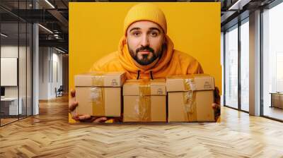 Delivery person in yellow uniform holding packages against yellow background Wall mural