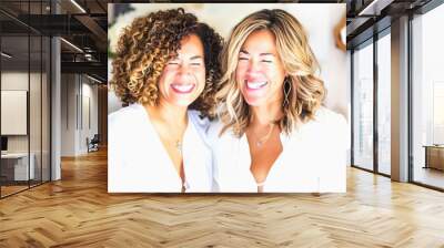 Two smiling women with curly and straight hair, wearing white shirts Wall mural