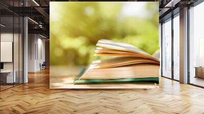 Open book on a wooden table in a garden. Sunny summer day, reading in a vacation concept Wall mural