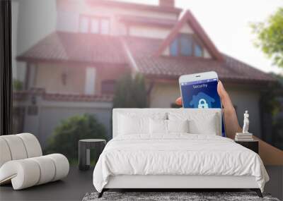 Smartphone with home security app in a hand on the building background Wall mural