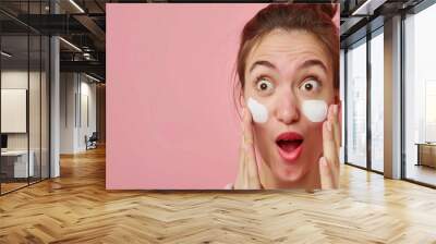 A women wondered by applying a cream by two fingers on her face on solid background pink color makeup Wall mural