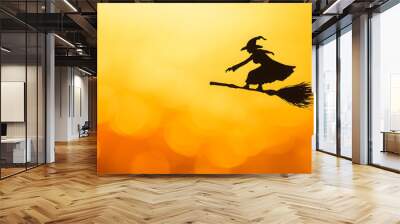 Silhouette of a witch flying on a broomstick against a vibrant orange backdrop. Wall mural