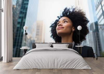 Low angle profile of confident and professional young African American black female businesswoman looking up while standing among skyscrapers. Wall mural