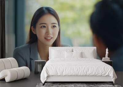 Smiling Korean or Japanese Asian woman sitting across from one man and talking. Meeting, conversation, counseling, consulting, interview concept. Professional business woman or female worker model. Wall mural