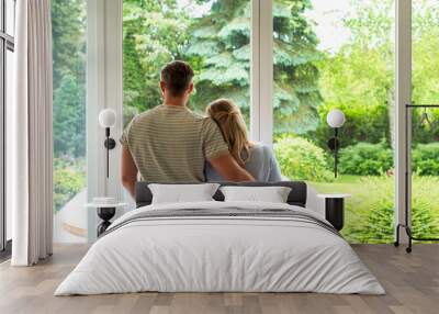 A couple standing at the window at home and looking out Wall mural