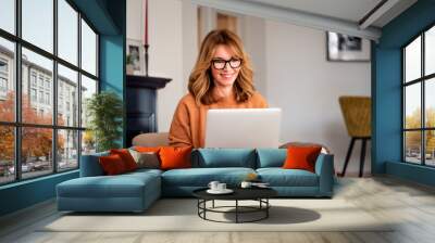 Casual woman sitting at home and using laptop for work Wall mural