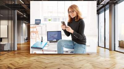 Creative businesswoman wearing casual dress while sitting at office desk and text messaging Wall mural