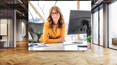 Middle aged businesswoman sitting behind her computer while working from home Wall mural