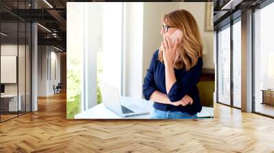 Middle aged businesswoman using mobile phone while working at home Wall mural