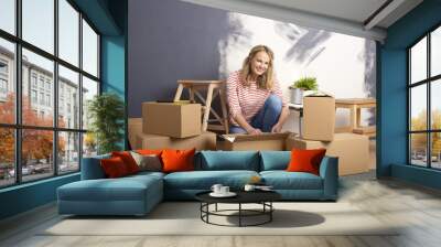 Moving in a new home. Portrait of a happy middle aged woman sitting in his new home surrounded by cardboard boxes. Wall mural