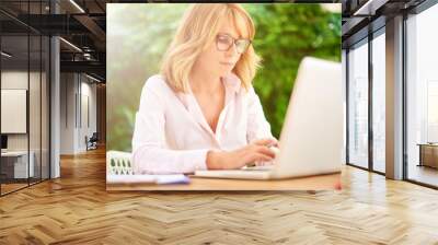 Portrait of concentrating woman sitting behind her laptop and working outside. Home office.  Wall mural