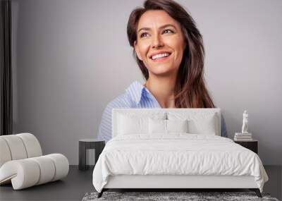 Studio portrait of attractive woman wearing shirt and laughing while sitting at isolated grey background. Wall mural