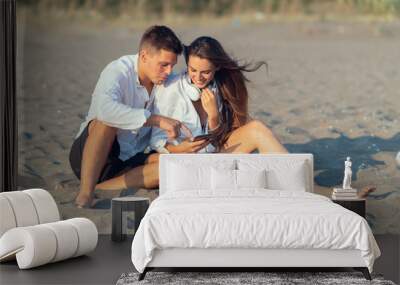 Young couple in love using smart phone on the beach  Wall mural