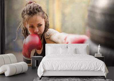 Woman boxer with tatto arms at workout. Young woman is boxing punching bag from car tires. At the head of the girl dreadlocks. Toned photo. Wall mural