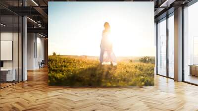 Young romantic woman on the meadow at sunset. The girl in the white dress enjoys the outdoors. Warm light . Strong glow of the sun behind the girl Wall mural