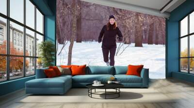 young woman athlete in black sport suit run in winter park Wall mural