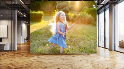 Child whirling, dancing plays on the meadow. Girl having fun with bubbles. Cute little longhair blonde girl dancing with soap bubbles at sunset park Wall mural