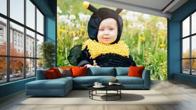 cute and cheerful portrait of little child sitting in blooming flowers of dandelion in yellow bee costume. concept nature and imagination. baby girl dressed as a bee. honey allergy. summer mood Wall mural